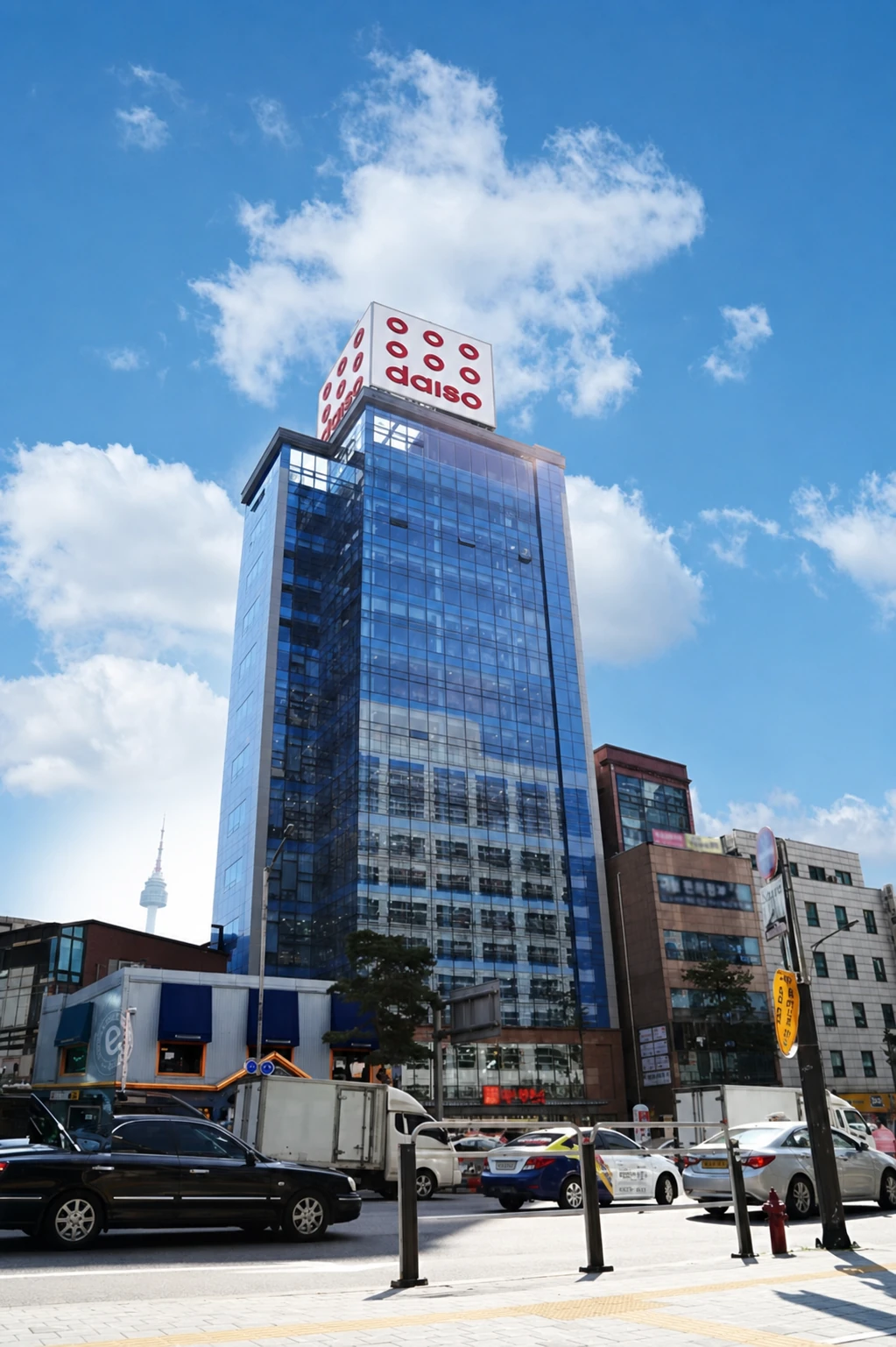 The narrow twelve-story glass building of Daiso Myeongdong Station with its red cube sign above the Seoul street